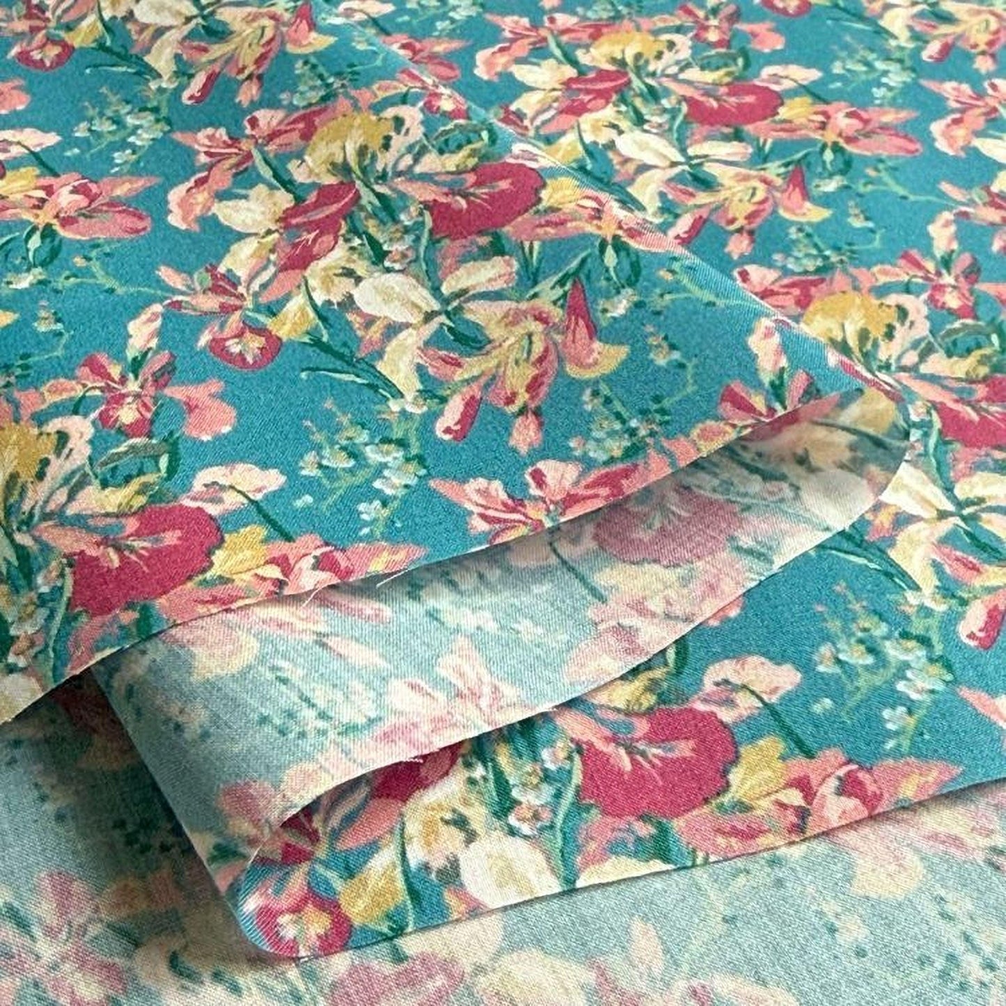 a close-up view of a fabric with a vibrant floral pattern in shades of blue, pink, and yellow. The fabric appears to be folded or rolled, revealing the intricate design of the flowers.