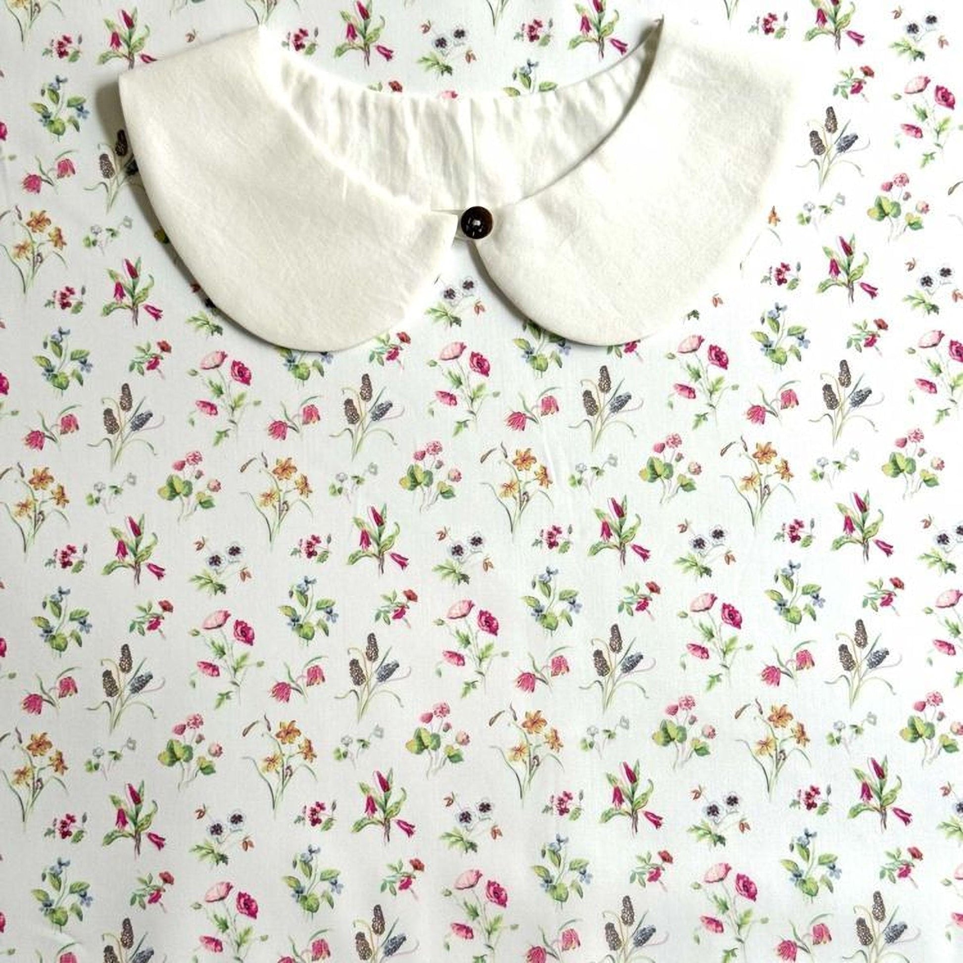 a white collar with a button, placed on a white fabric with a floral pattern.
