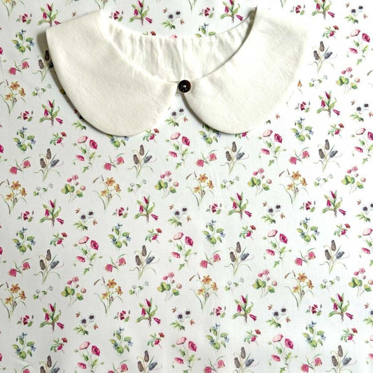 a white collar with a button, placed on a white fabric with a floral pattern.
