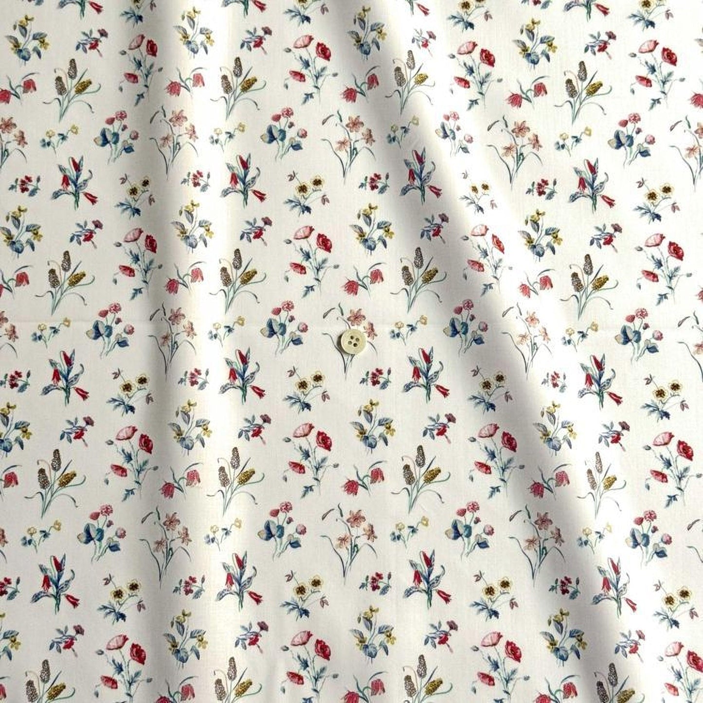 a close-up view of a fabric with a repeating floral pattern in various colors, including red, blue, yellow, and green. The pattern consists of small flowers and leaves, creating a visually appealing and intricate design.