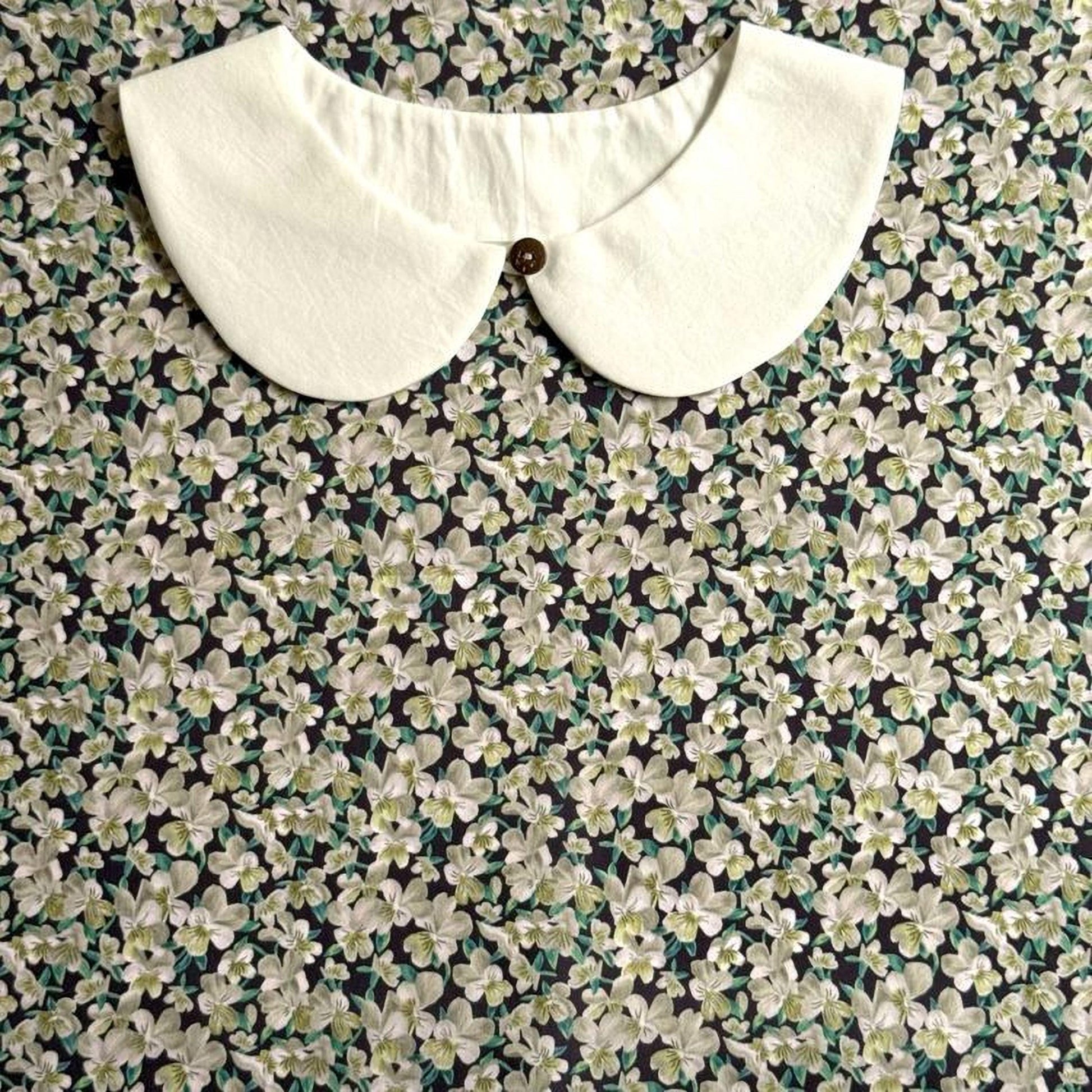 a white collar with a button, set against a background of a floral print fabric.