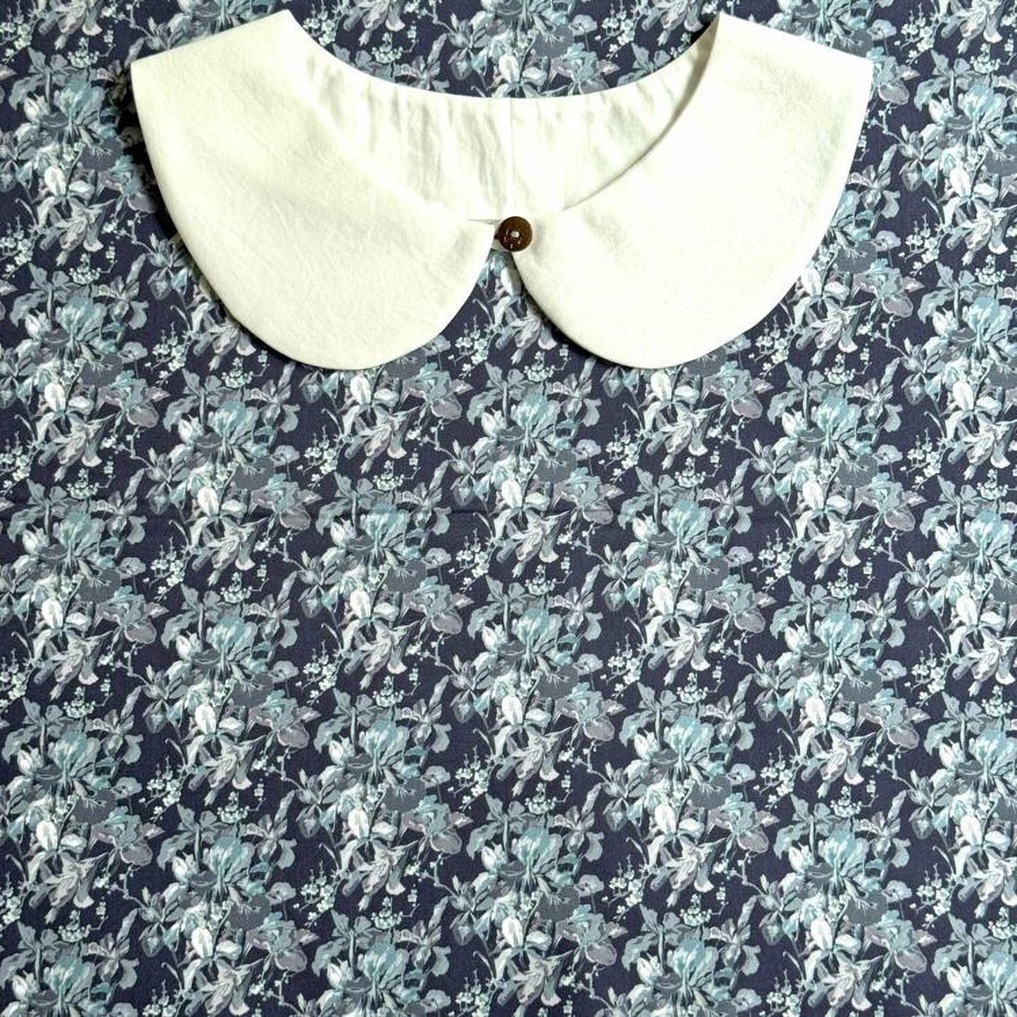 a white collar with a button, set against a background with a blue and white floral pattern.