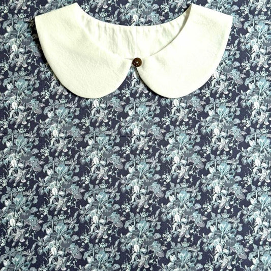 a white collar with a button, set against a background with a blue and white floral pattern.