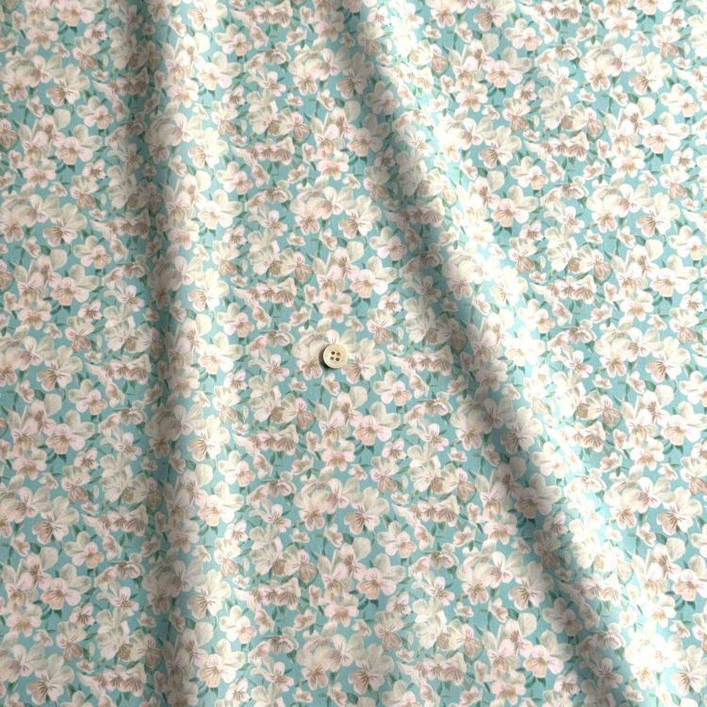 a close-up view of a fabric with a floral pattern in shades of blue and white. The fabric appears to be made of a soft, light-colored material, possibly cotton or linen. There is a small button visible in the center of the fabric.