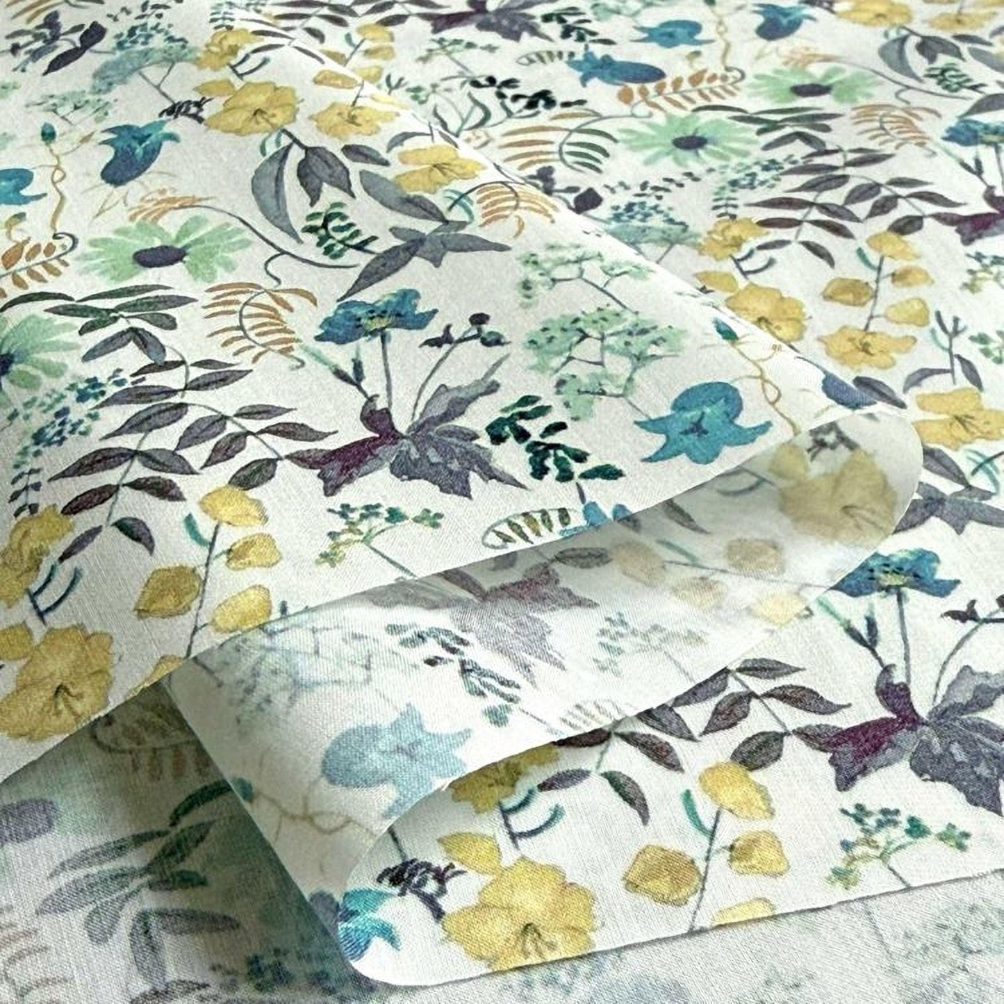 a close-up view of a fabric with a floral pattern, including yellow flowers and green leaves. The fabric appears to be a white material with a printed design.