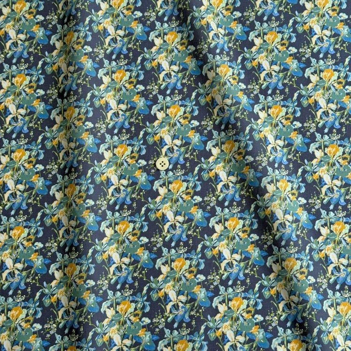 a close-up view of a fabric with a floral pattern in shades of blue, yellow, and green. The pattern is intricate and detailed, with the flowers and leaves filling the entire fabric. The fabric appears to be a dark blue color, providing a contrast to the vibrant colors of the flowers. The fabric is folded and crumpled, giving it a slightly wrinkled appearance.