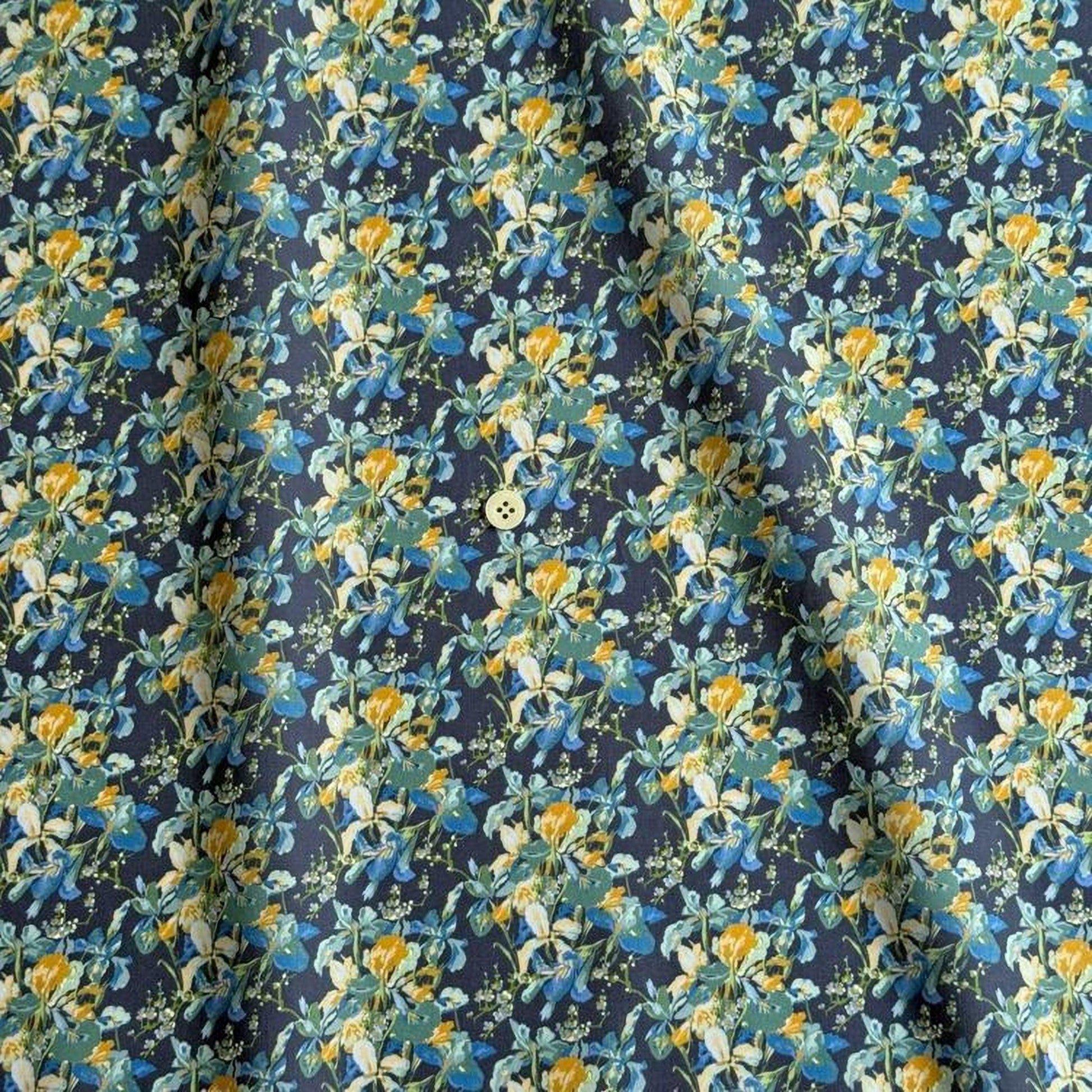 a close-up view of a fabric with a floral pattern in shades of blue, yellow, and green. The pattern is intricate and detailed, with the flowers and leaves filling the entire fabric. The fabric appears to be a dark blue color, providing a contrast to the vibrant colors of the flowers. The fabric is folded and crumpled, giving it a slightly wrinkled appearance.