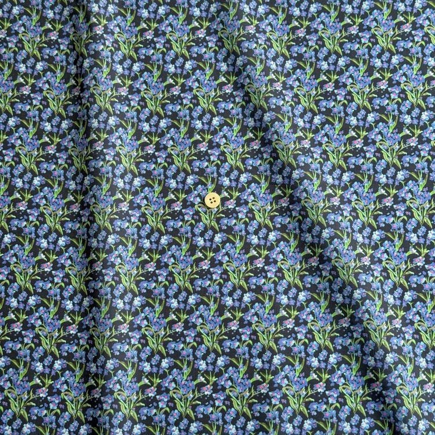 a close-up view of a fabric with a repeating pattern of blue flowers on a dark background. There is a single yellow button visible in the center of the fabric.