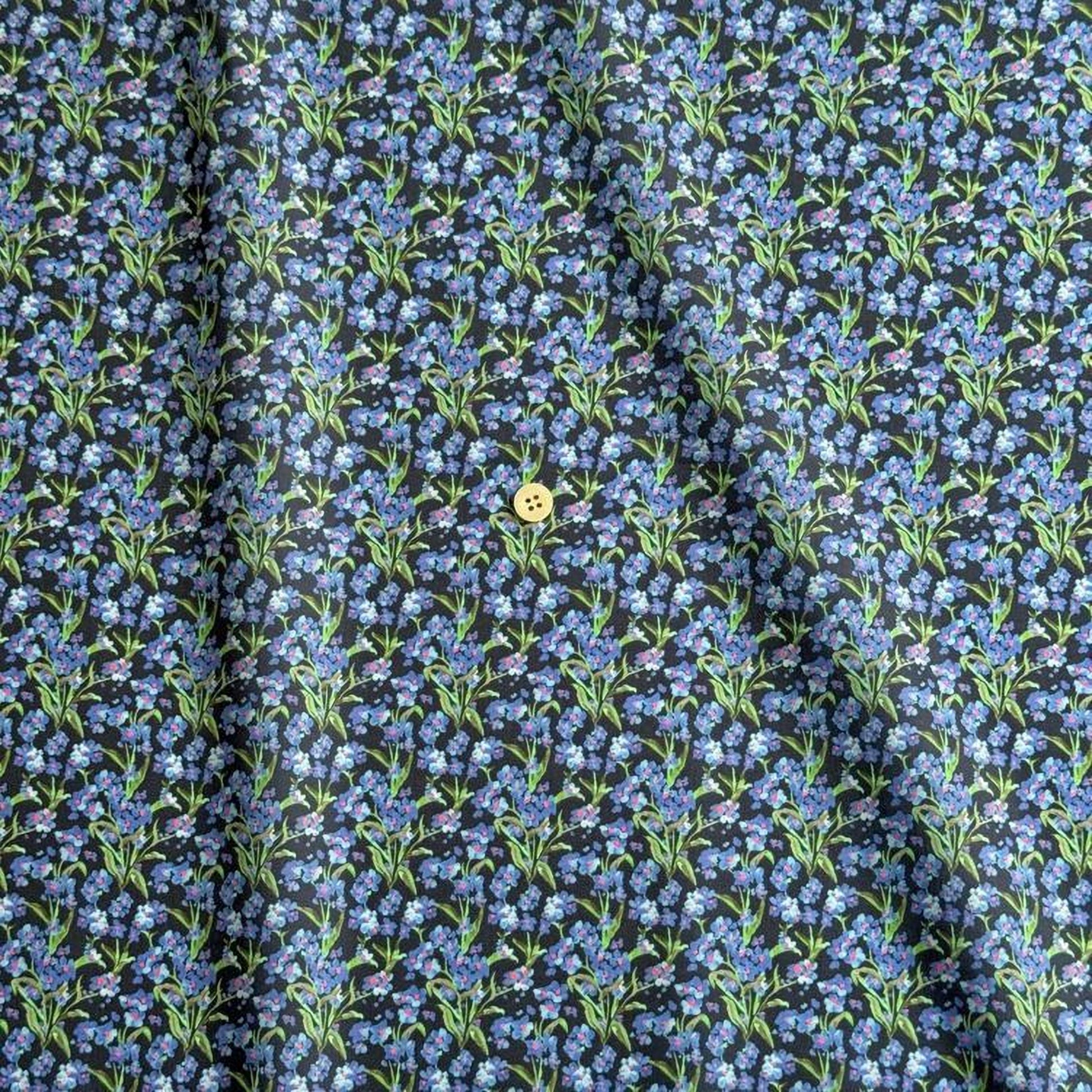 a close-up view of a fabric with a repeating pattern of blue flowers on a dark background. There is a single yellow button visible in the center of the fabric.