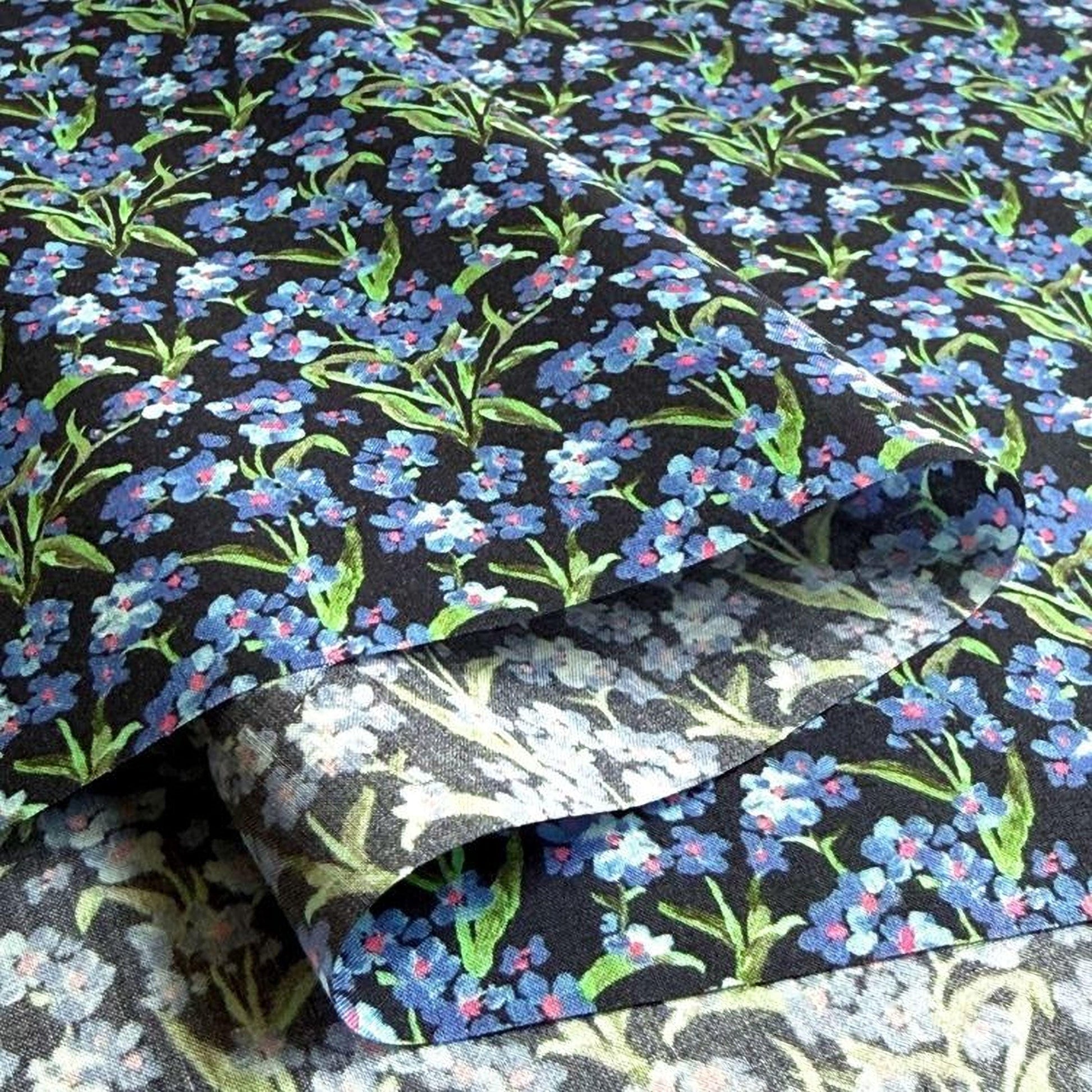 a close-up view of a fabric with a floral pattern in shades of blue and green. The fabric appears to be folded or rolled, revealing the intricate design of the flowers and leaves.
