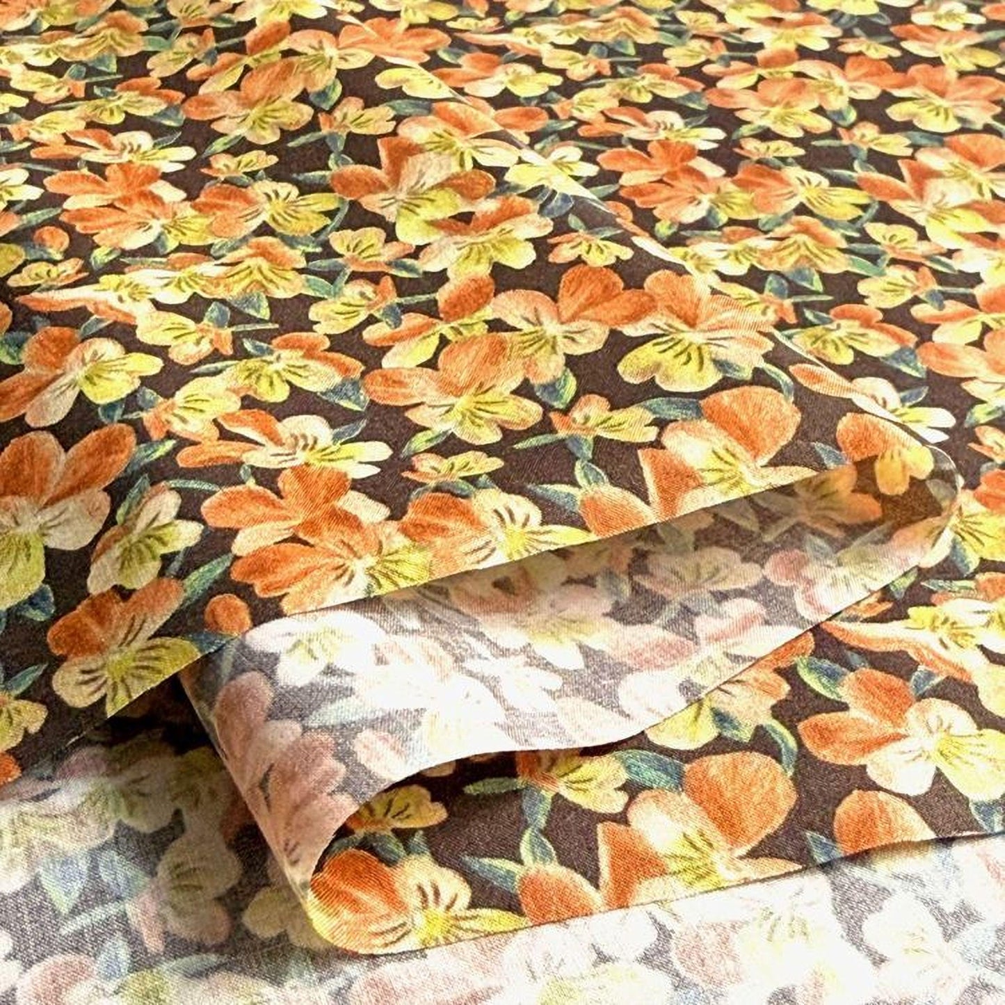 a close-up view of a fabric with a floral pattern, showcasing a variety of orange and yellow flowers against a dark background.