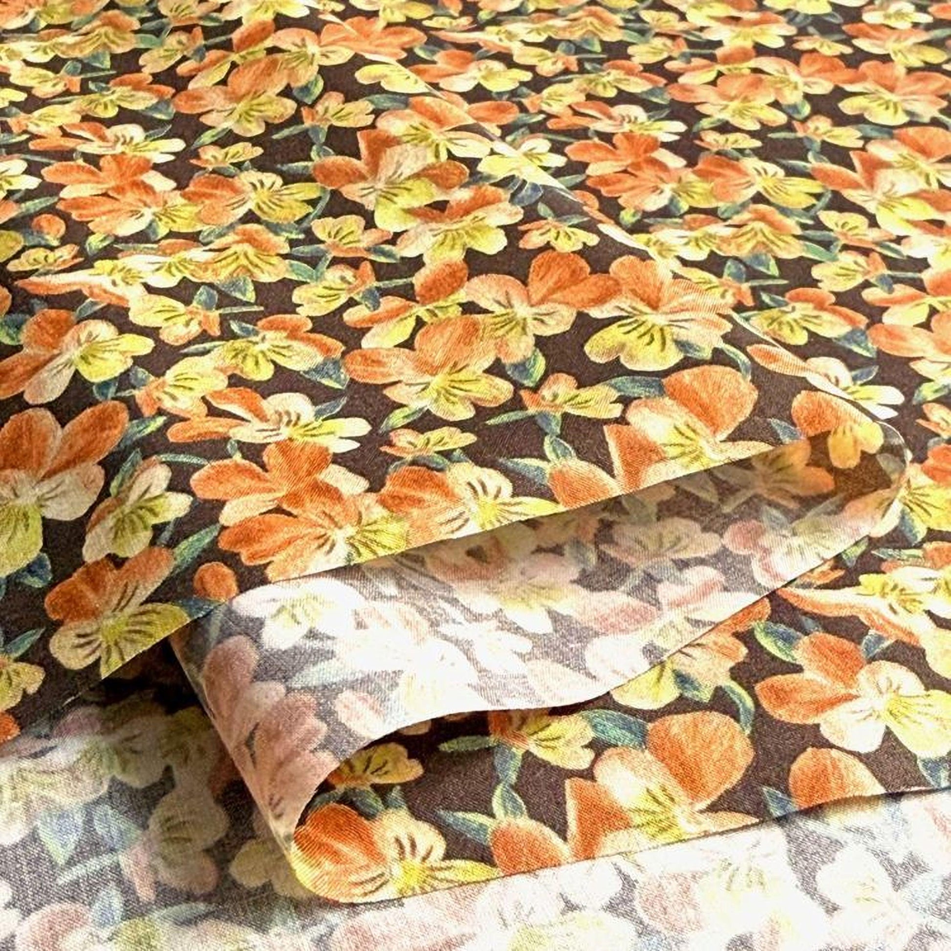 a close-up view of a fabric with a floral pattern, showcasing a variety of orange and yellow flowers against a dark background.