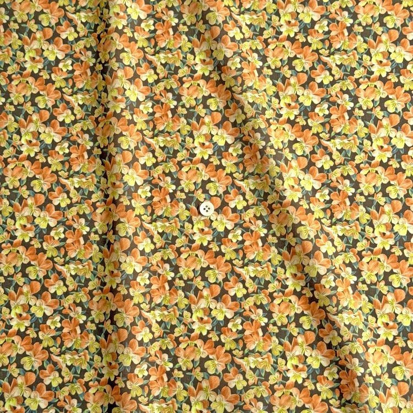 a close-up view of a fabric with a floral pattern in shades of orange and yellow. The fabric appears to be made of a soft, textured material, and there is a small white button visible in the center of the pattern.
