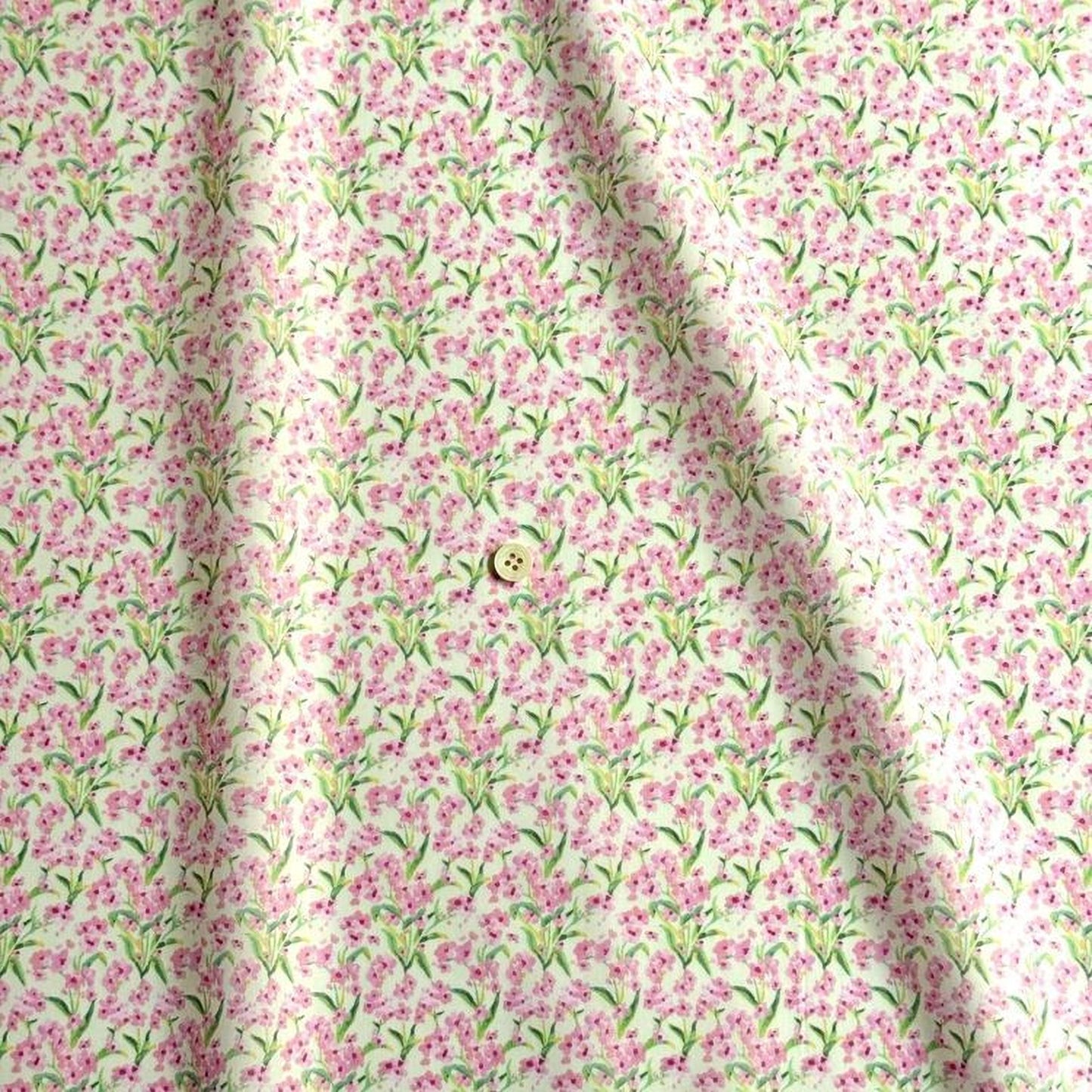 a fabric with a repeating pattern of pink flowers and green leaves. The fabric appears to be made of a soft, light-colored material. There is a small button visible in the center of the fabric.