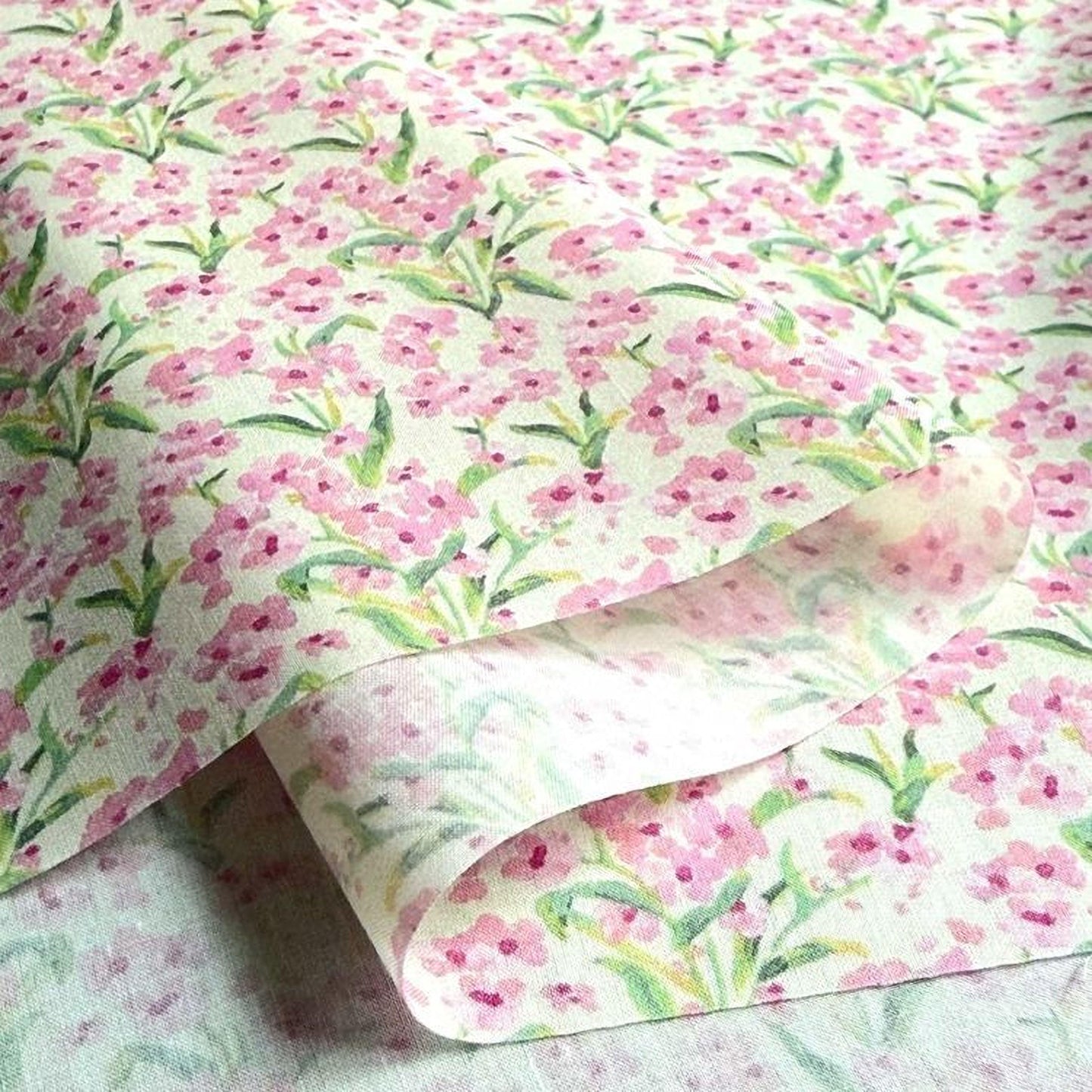 a close-up view of a fabric with a floral pattern, featuring pink flowers and green leaves. The fabric appears to be folded or rolled, revealing the intricate design underneath.