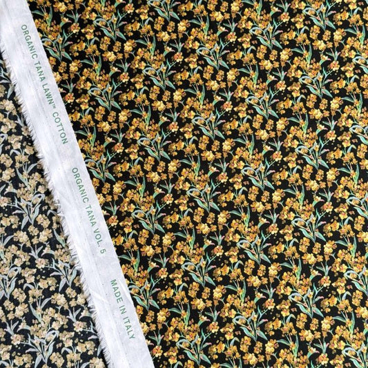 a close-up view of a fabric with a floral pattern, including yellow flowers and green leaves. The fabric appears to be made of organic cotton and is displayed alongside a white label that reads "Organic TANA LYNCH COTTON VOL. 5 MADE IN ITALY".