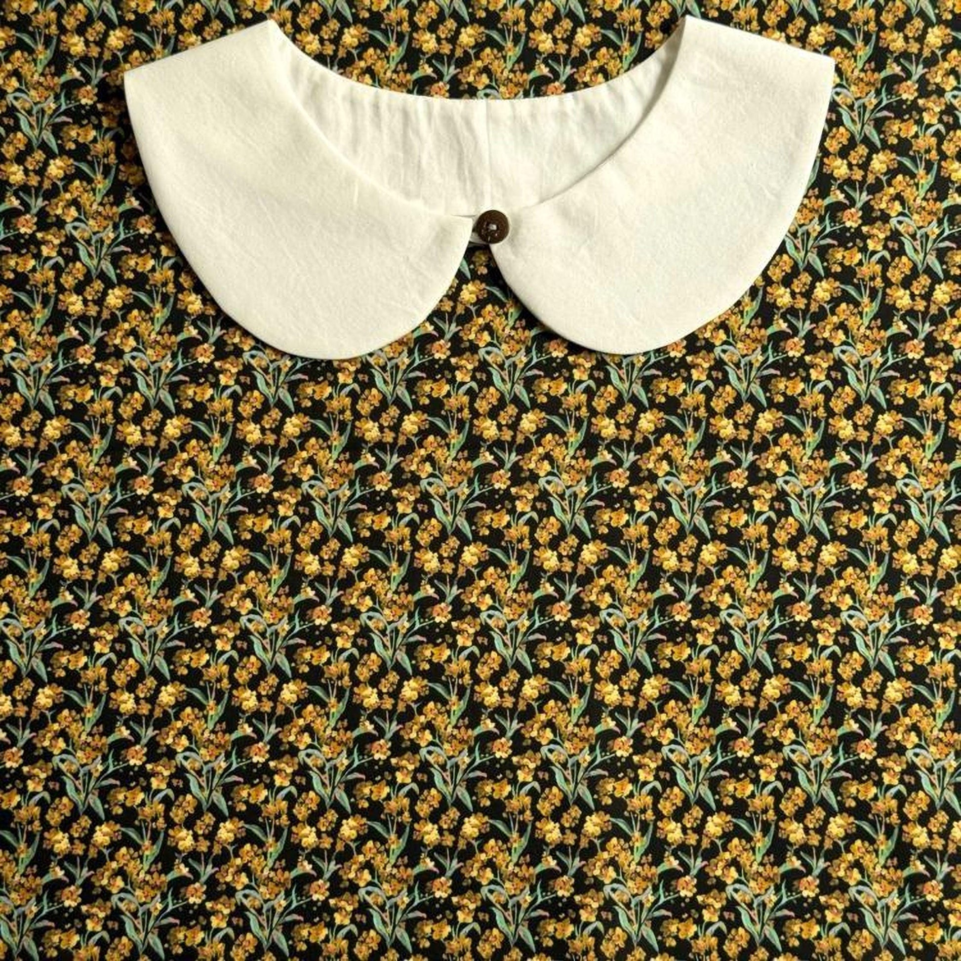 A white collar is displayed against a background of a black and yellow floral print.