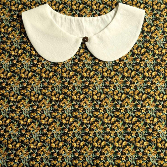 A white collar is displayed against a background of a black and yellow floral print.