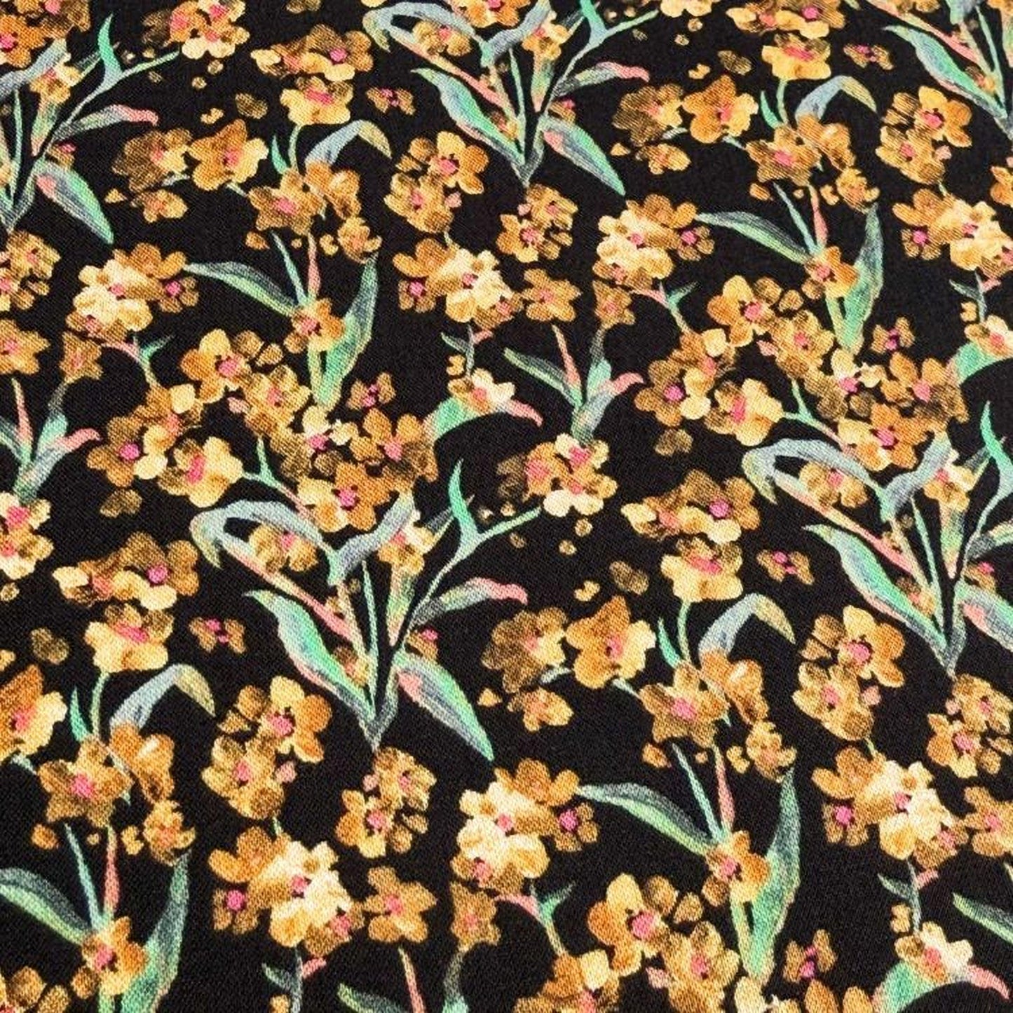 a close-up view of a fabric with a floral pattern. The fabric is predominantly black, with yellow flowers and green leaves scattered across it. The pattern is intricate and detailed, showcasing the craftsmanship of the design.