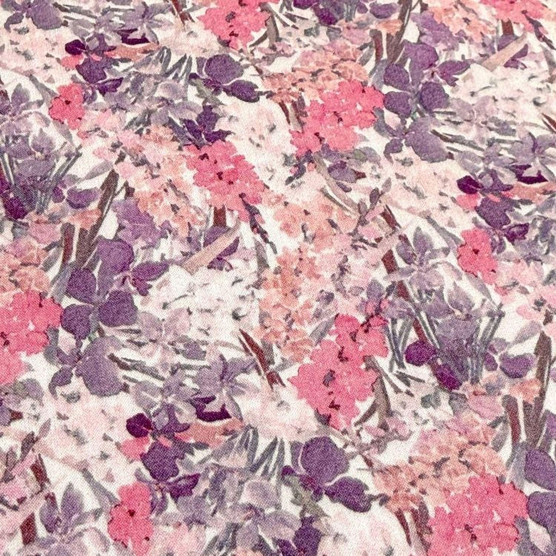 The image is a close-up of a fabric with a floral pattern in shades of pink, purple, and white. The pattern consists of various flowers and leaves, creating a visually appealing and intricate design.