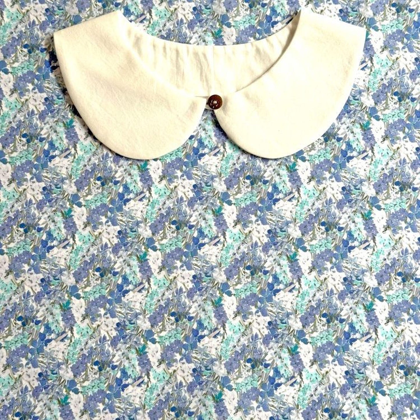 a white collar with a button, set against a background of a blue and white floral print.