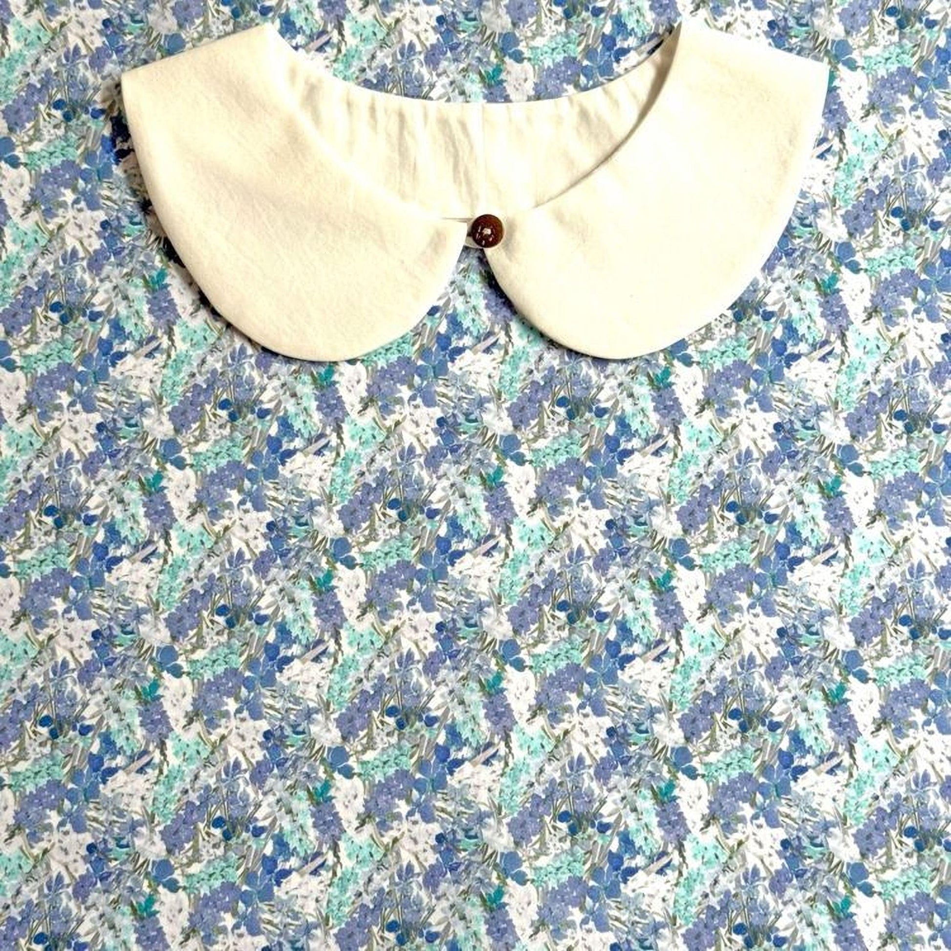 a white collar with a button, set against a background of a blue and white floral print.
