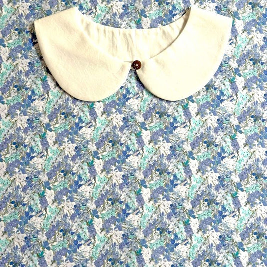 a white collar with a button, set against a background of a blue and white floral print.