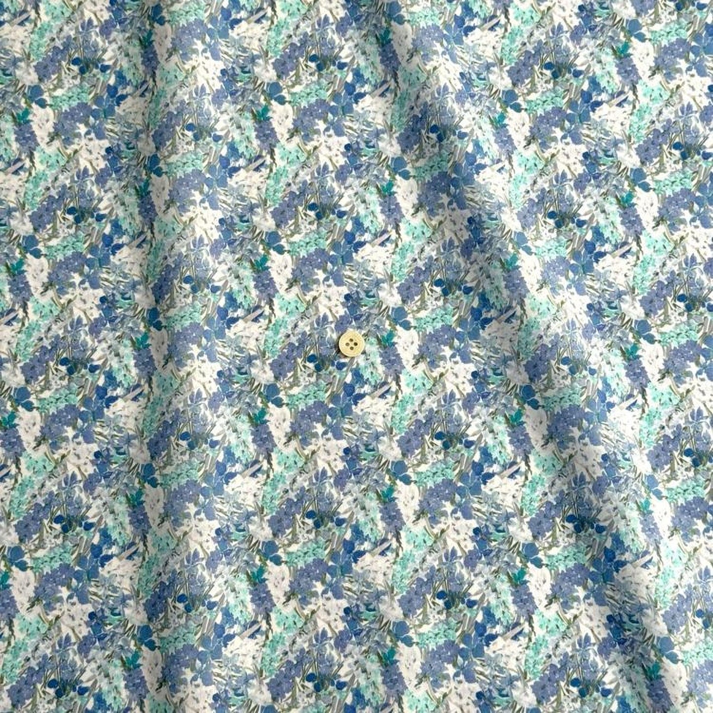 a close-up view of a fabric with a floral pattern in shades of blue and white. The fabric appears to be made of a soft, textured material, and there is a small button visible in the center of the fabric.