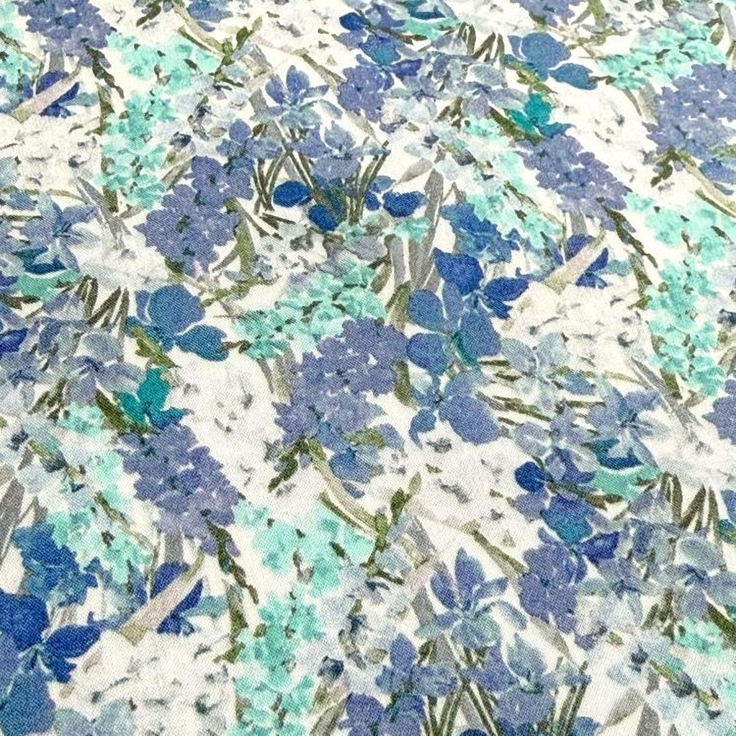 The image is a close-up of a fabric with a floral pattern in shades of blue and green. The pattern consists of various flowers and leaves, creating a visually appealing and intricate design.