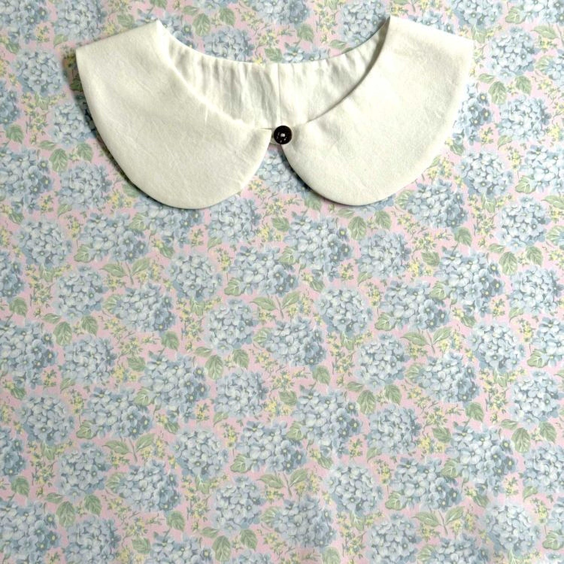 A white collar with a button is displayed against a floral print background.