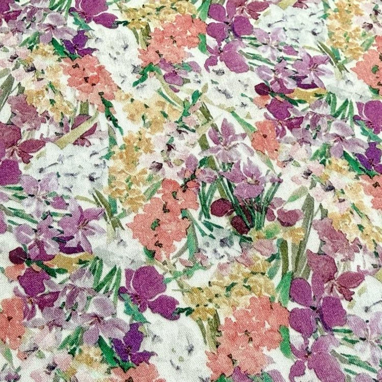 The image is a close-up of a fabric with a vibrant floral pattern, featuring a variety of colorful flowers and leaves in shades of pink, purple, yellow, and green.
