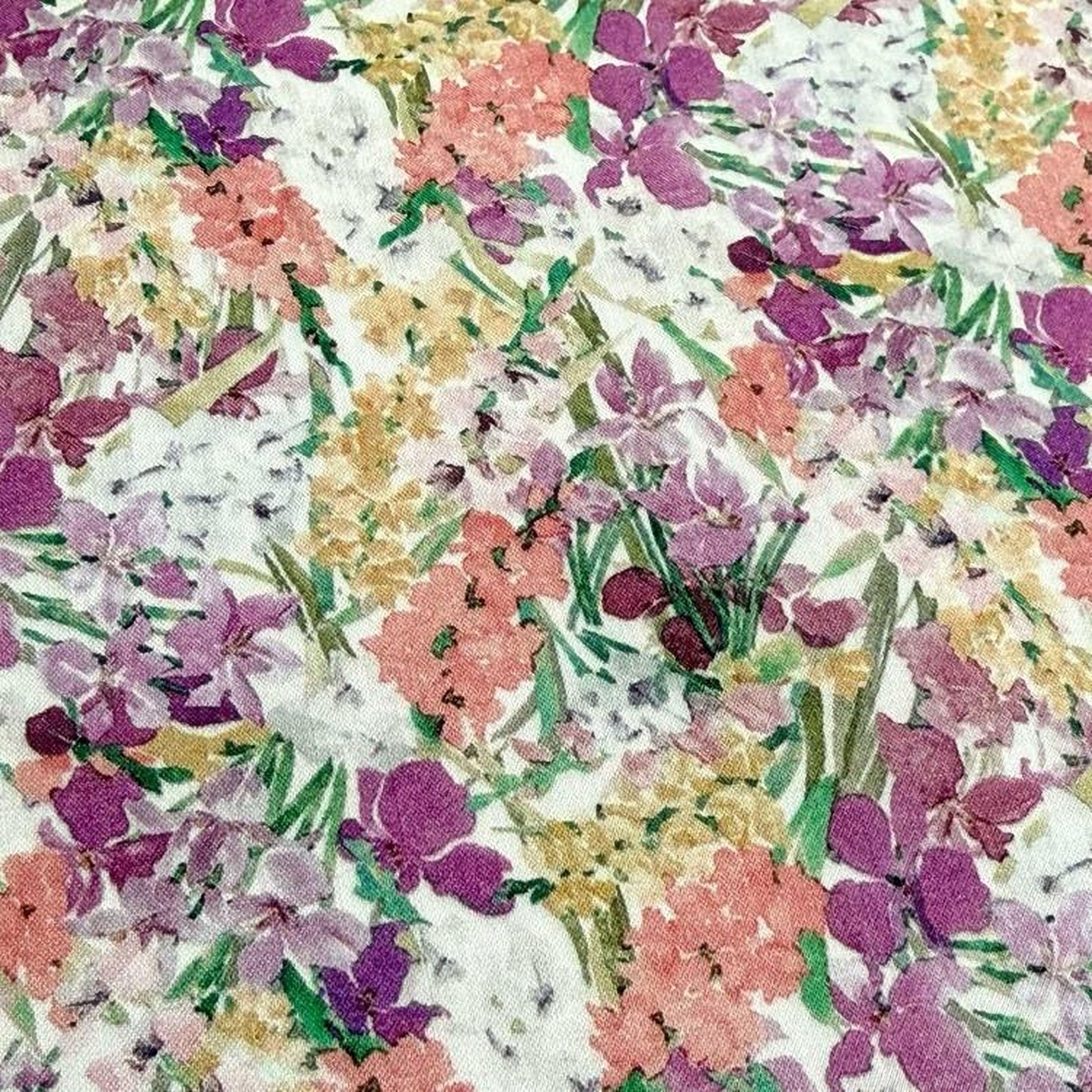 The image is a close-up of a fabric with a vibrant floral pattern, featuring a variety of colorful flowers and leaves in shades of pink, purple, yellow, and green.