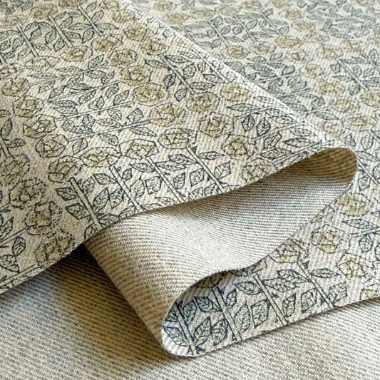 a close-up view of a fabric with a repeating pattern of leaves and flowers in shades of green and beige.