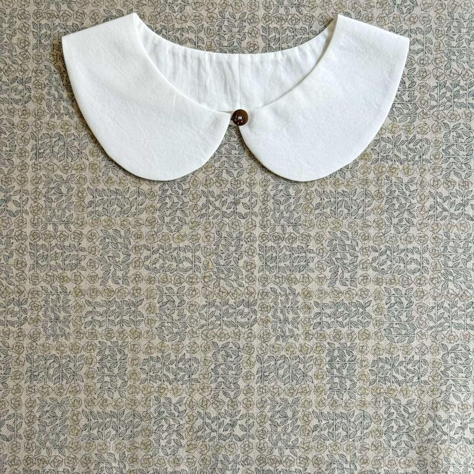 A white collar with a button is displayed against a patterned fabric background.