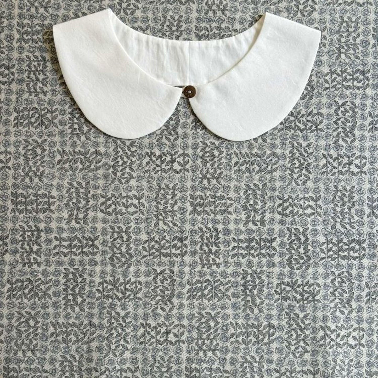 A white collar is displayed against a gray and white patterned fabric background.