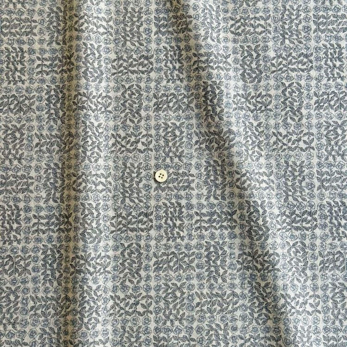 a close-up view of a fabric with a repeating pattern of gray and white floral designs. There is a small white button visible in the center of the fabric.