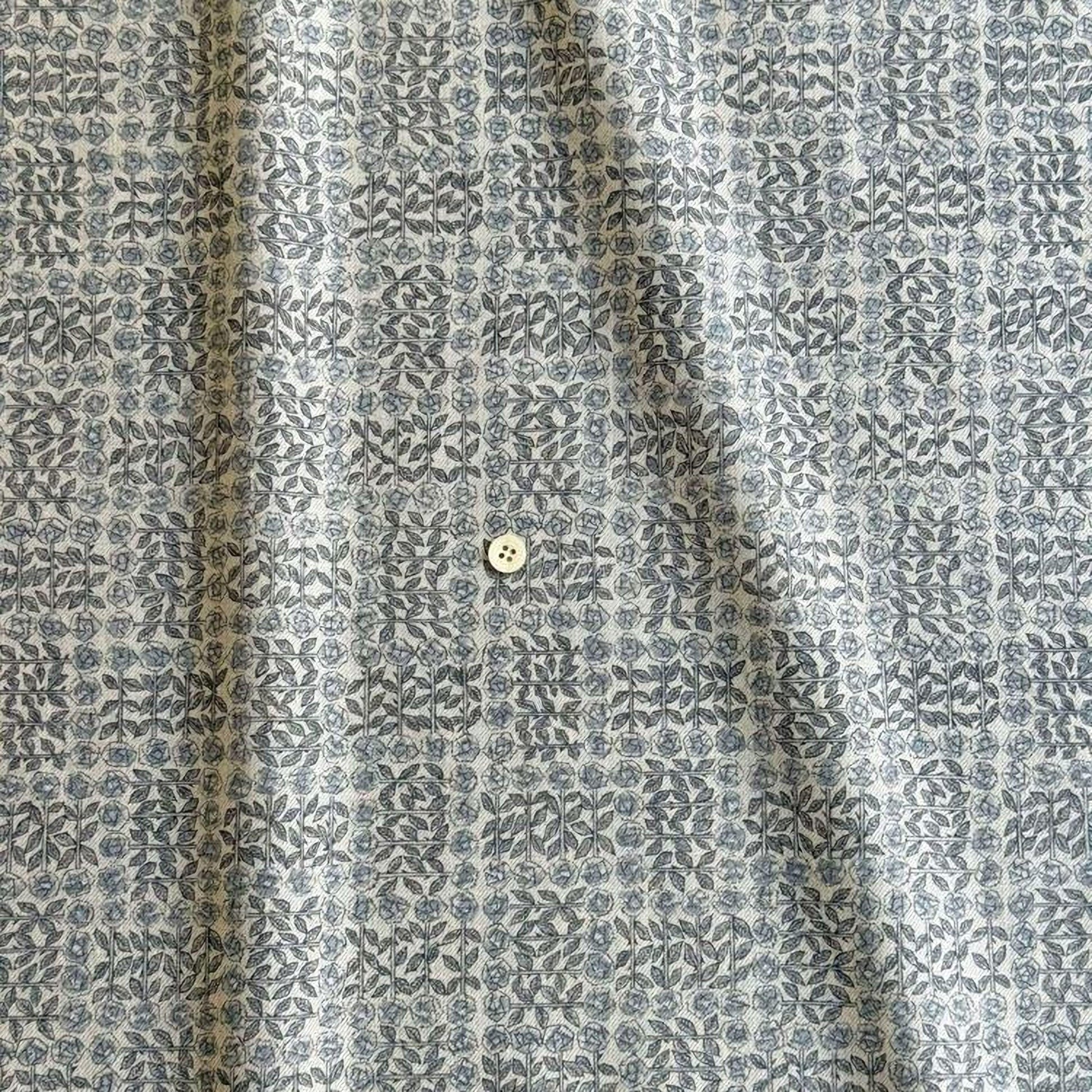 a close-up view of a fabric with a repeating pattern of gray and white floral designs. There is a small white button visible in the center of the fabric.