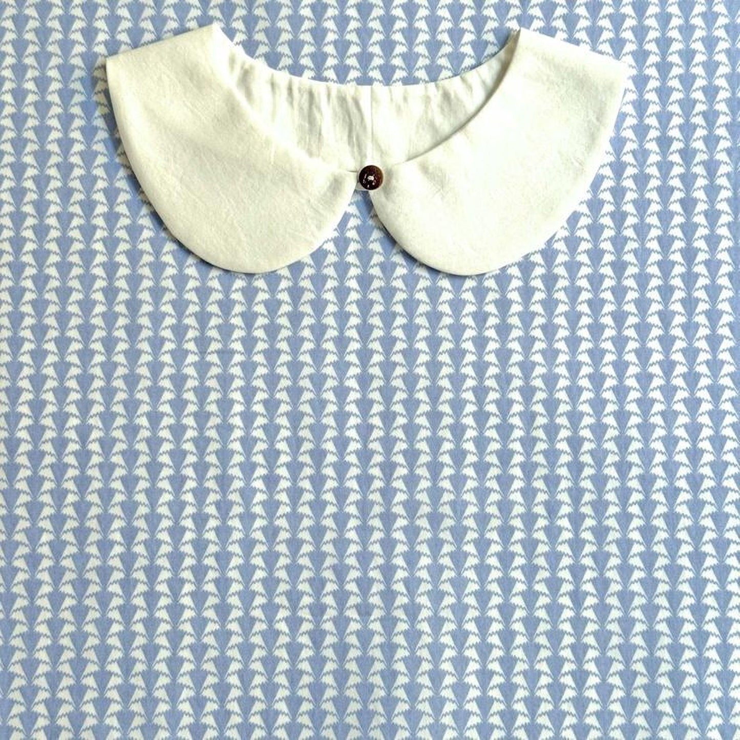 A white collar is displayed against a blue and white patterned background.