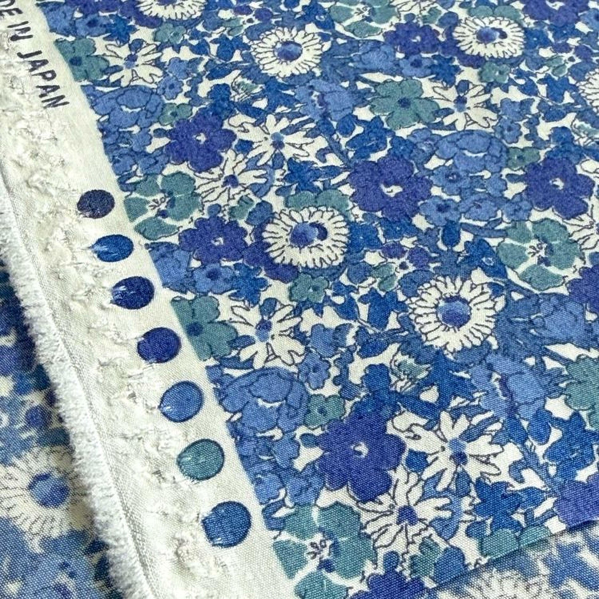 a close-up view of a fabric with a blue and white floral pattern. The fabric appears to be a piece of cloth or textile, with a repeating pattern of blue and white flowers and leaves. The fabric is folded and displayed, showcasing the intricate design and texture of the floral pattern.