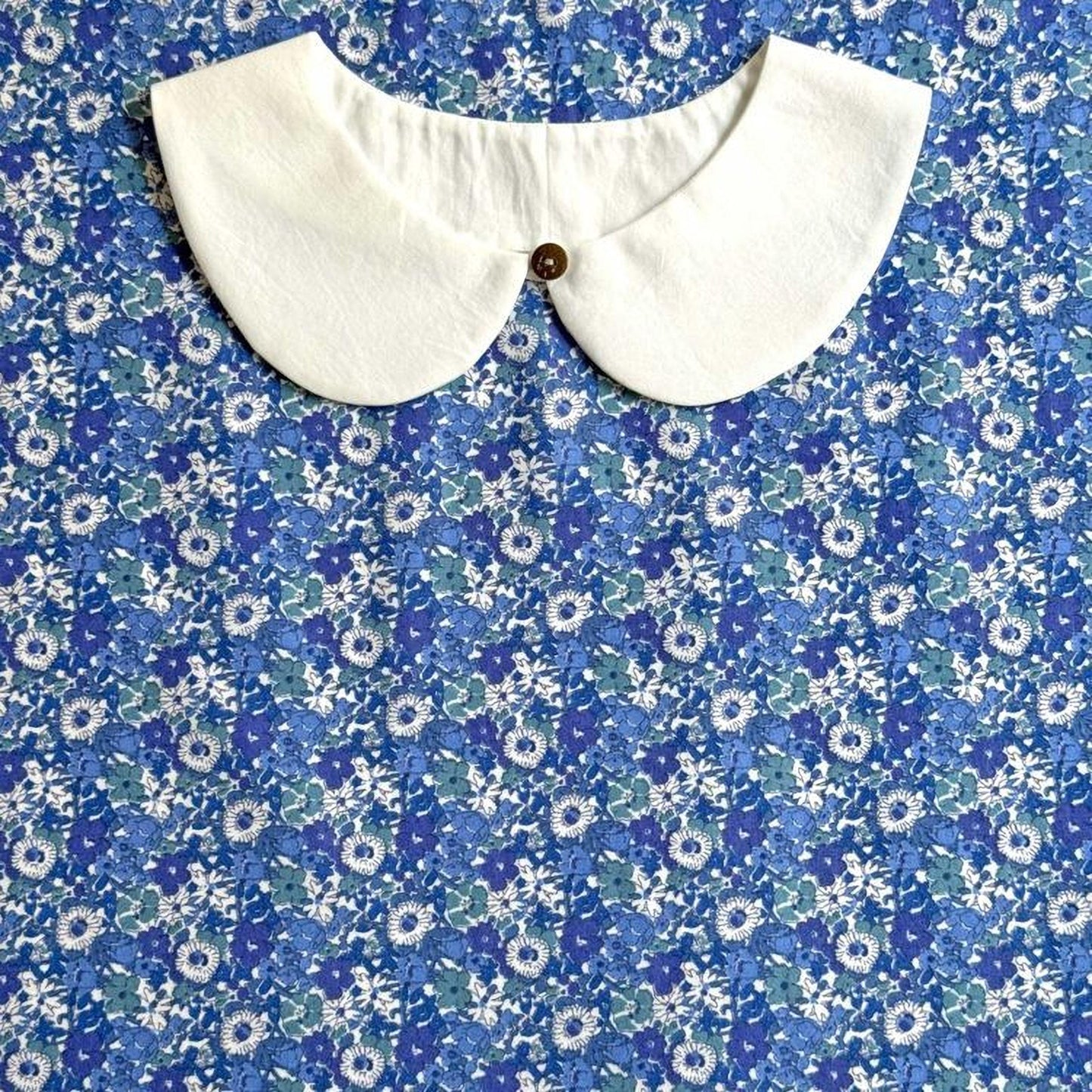 a white collar with a button, set against a blue and white floral patterned fabric.