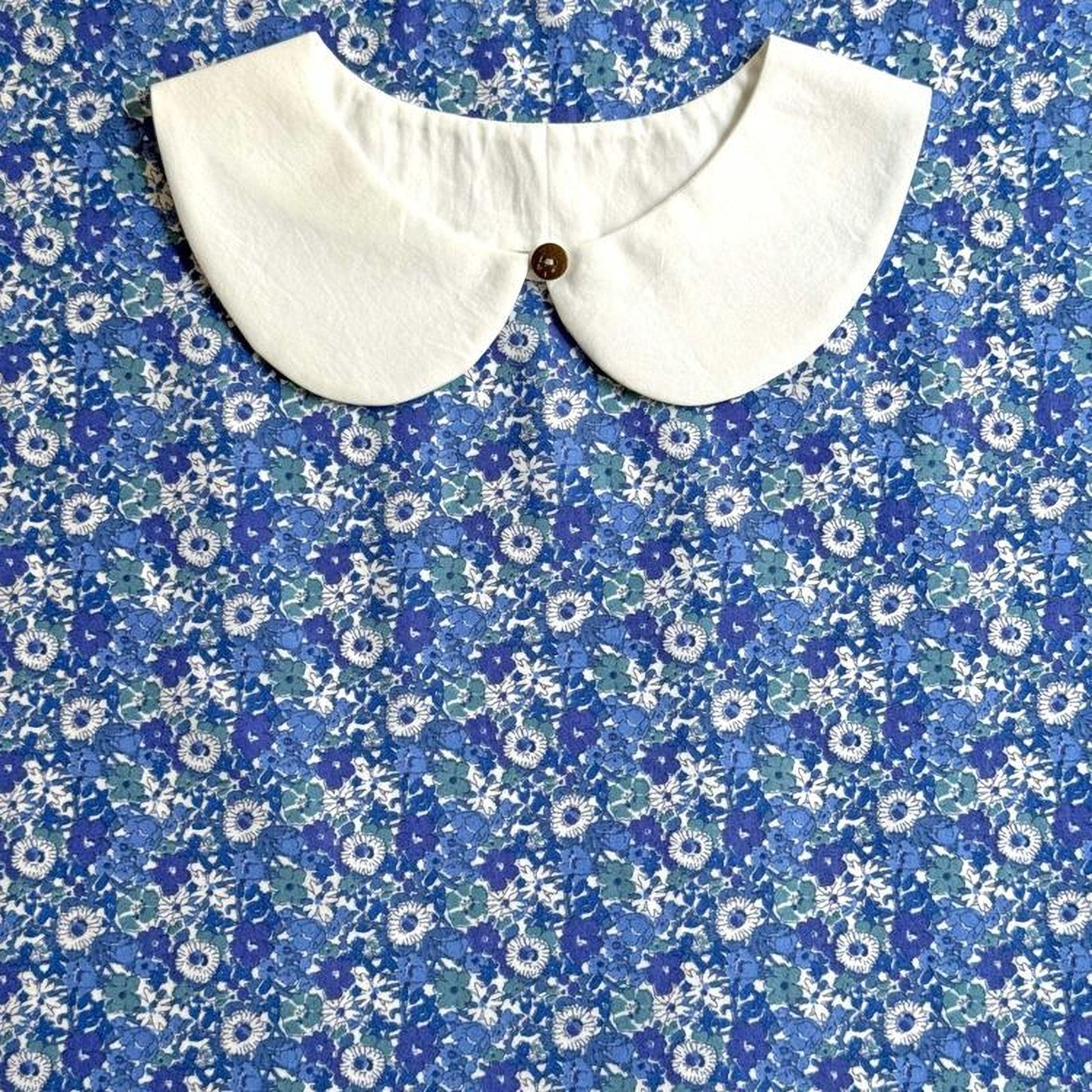 a white collar with a button, set against a blue and white floral patterned fabric.