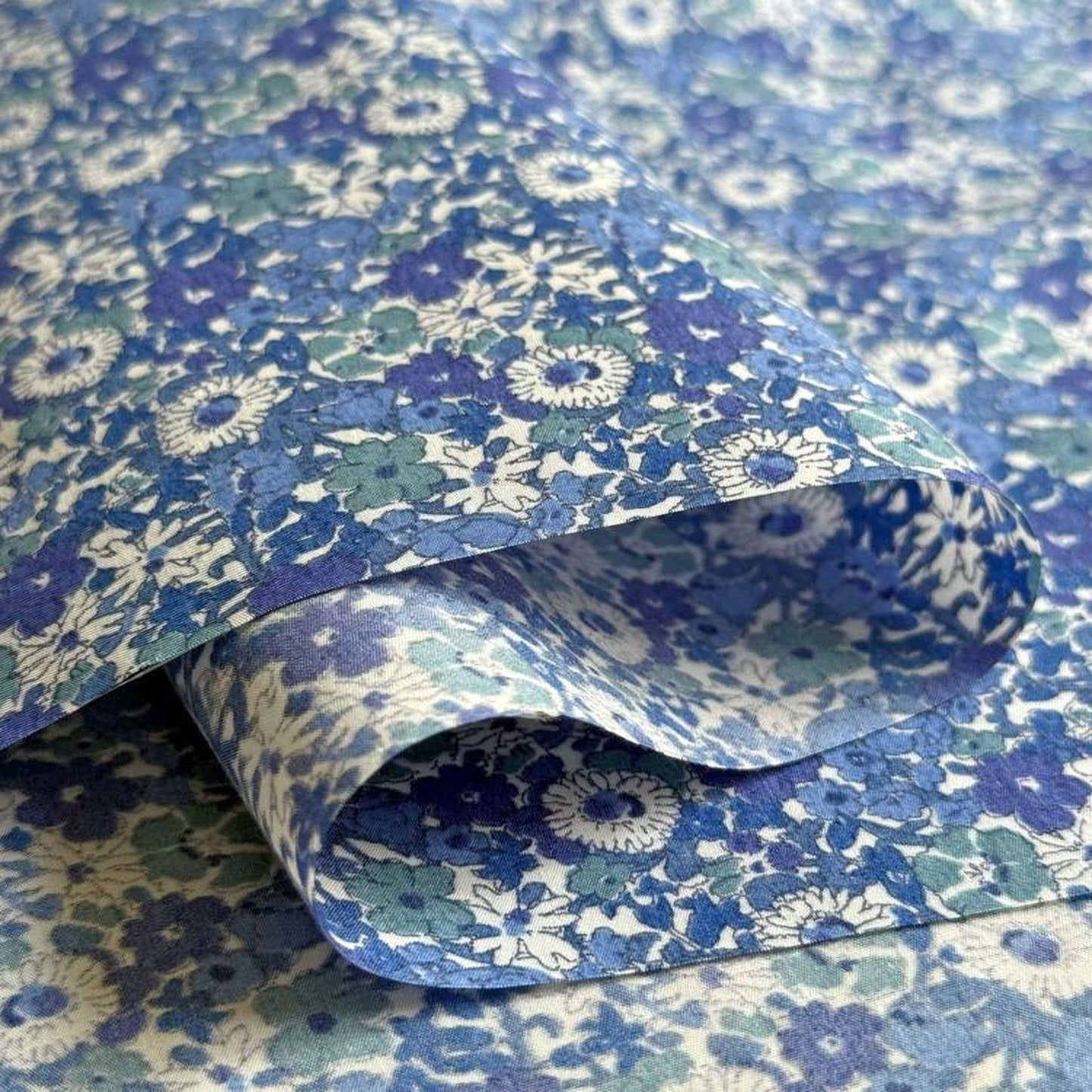 a close-up view of a fabric with a blue and white floral pattern. The fabric appears to be folded or rolled, revealing the intricate design of the flowers and leaves.