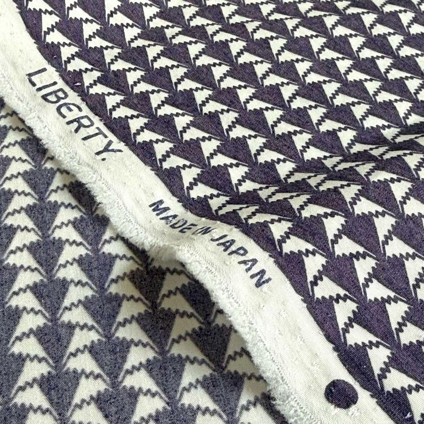 a close-up view of a fabric with a repeating pattern of triangles in shades of gray and white. The fabric appears to be made in Japan, as indicated by the text "MADE IN JAPAN" printed on it.
