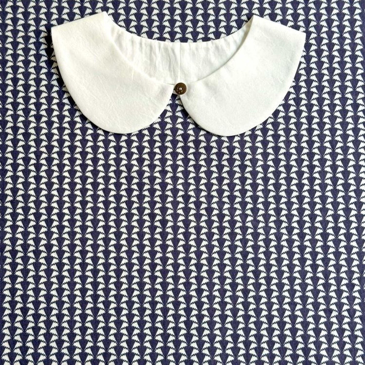 A white collar is displayed against a blue and white patterned fabric background.