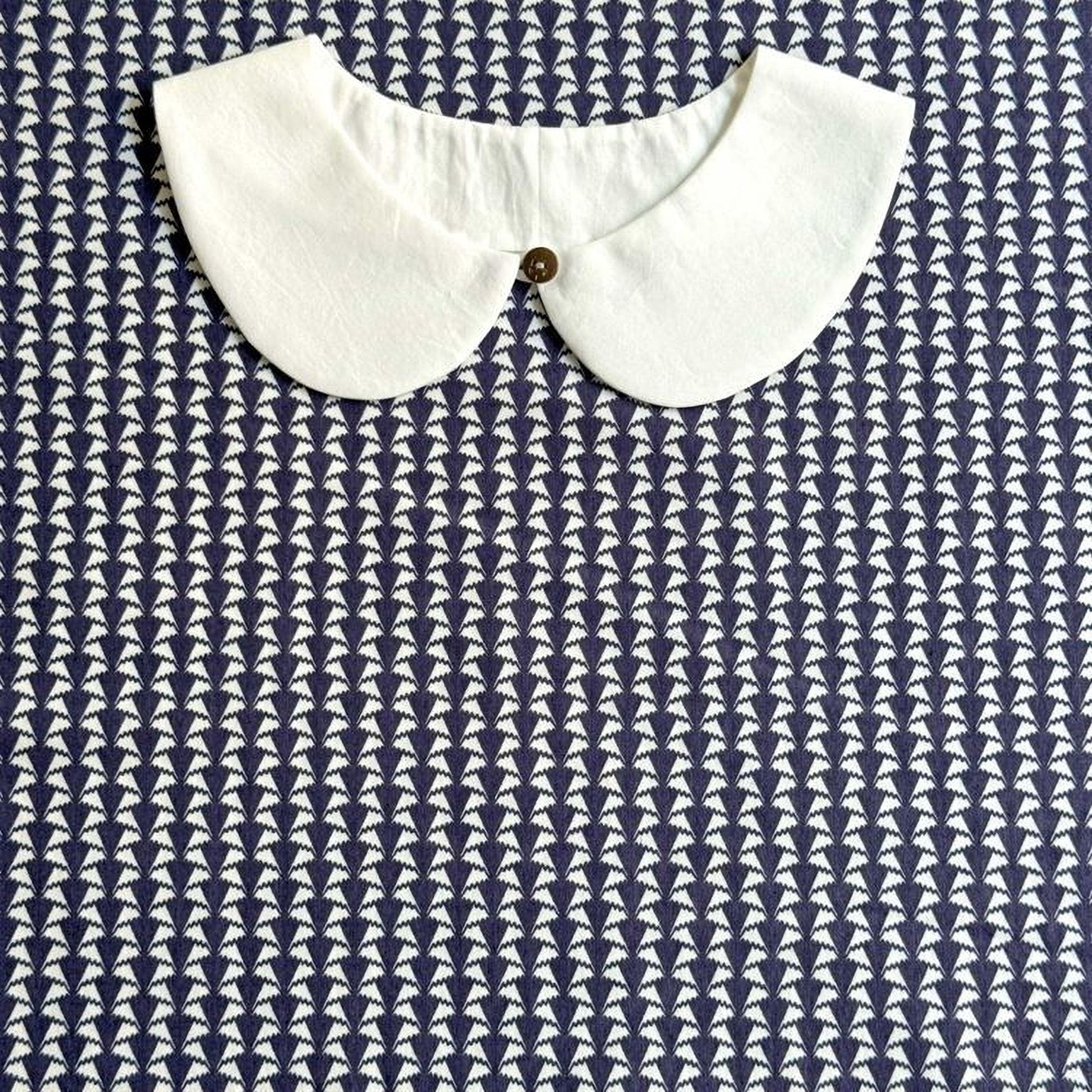 A white collar is displayed against a blue and white patterned fabric background.
