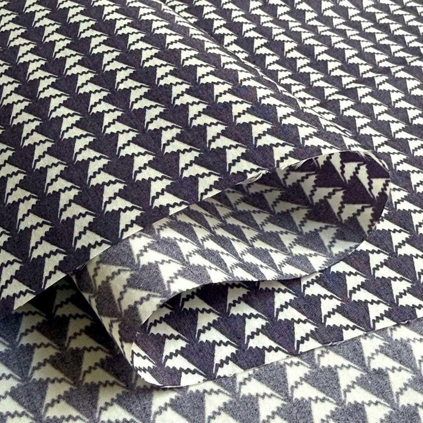 a close-up view of a fabric with a repeating pattern of black and white triangles. The pattern is intricate and detailed, with the triangles arranged in a diagonal line across the fabric. The fabric appears to be folded or rolled, revealing the intricate design underneath.