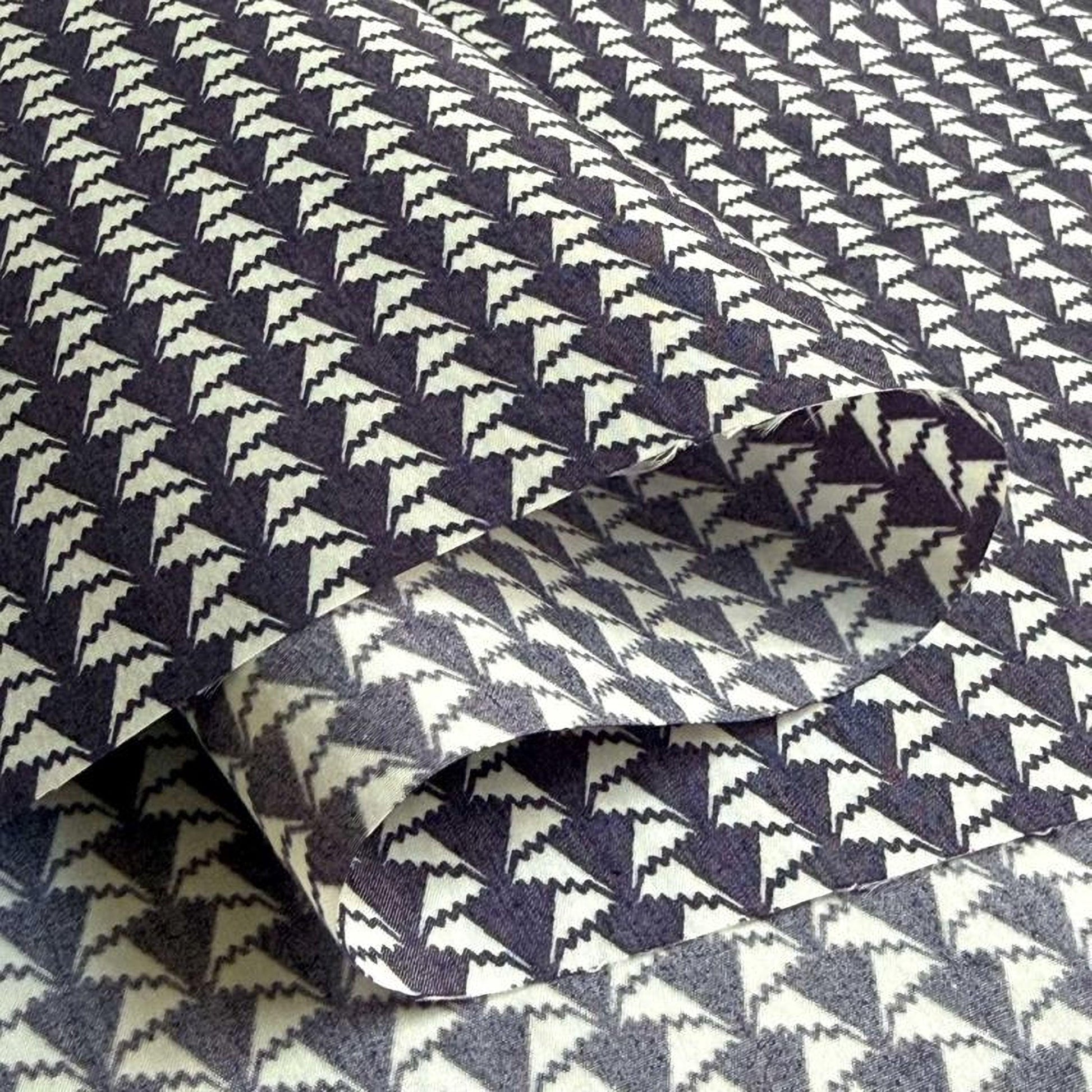 a close-up view of a fabric with a repeating pattern of black and white triangles. The pattern is intricate and detailed, with the triangles arranged in a diagonal line across the fabric. The fabric appears to be folded or rolled, revealing the intricate design underneath.