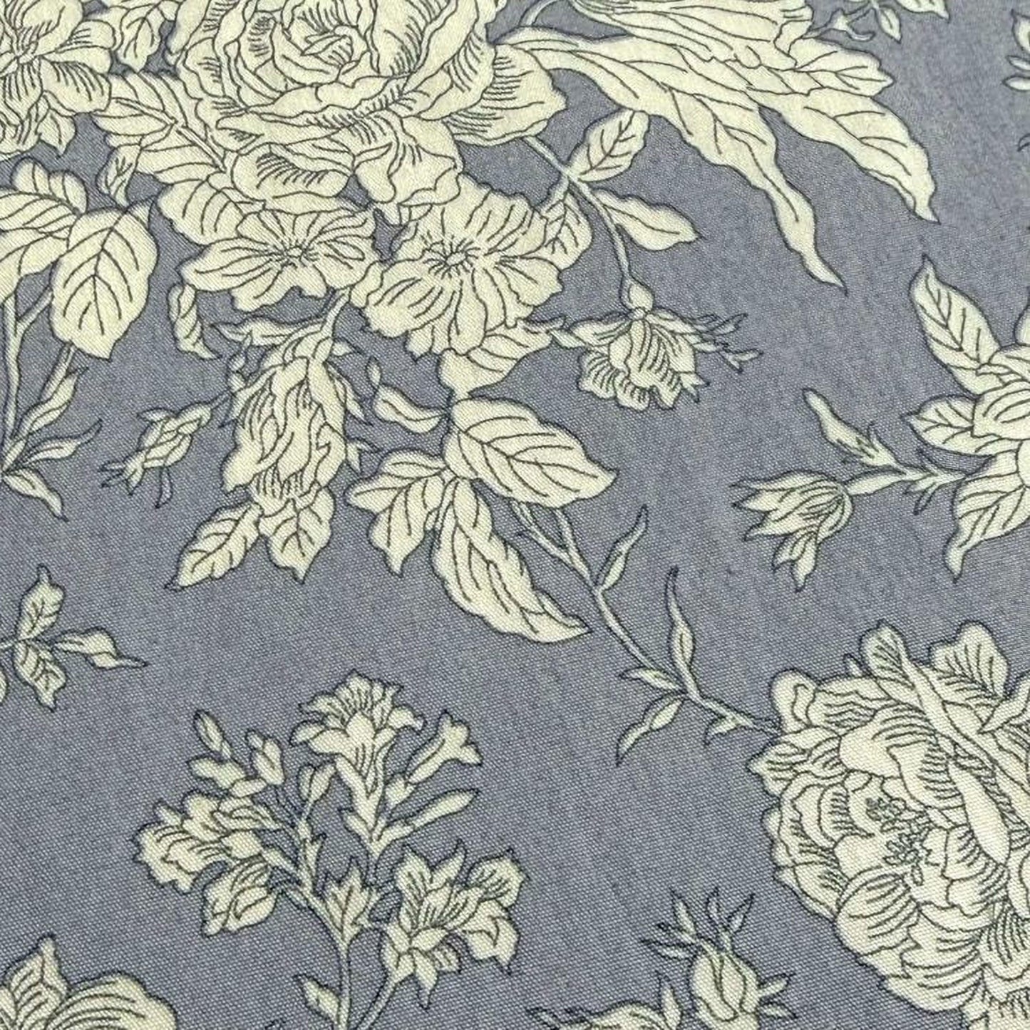 a close-up view of a fabric with a floral pattern in shades of gray and white. The pattern consists of various flowers and leaves, creating a visually appealing and intricate design.