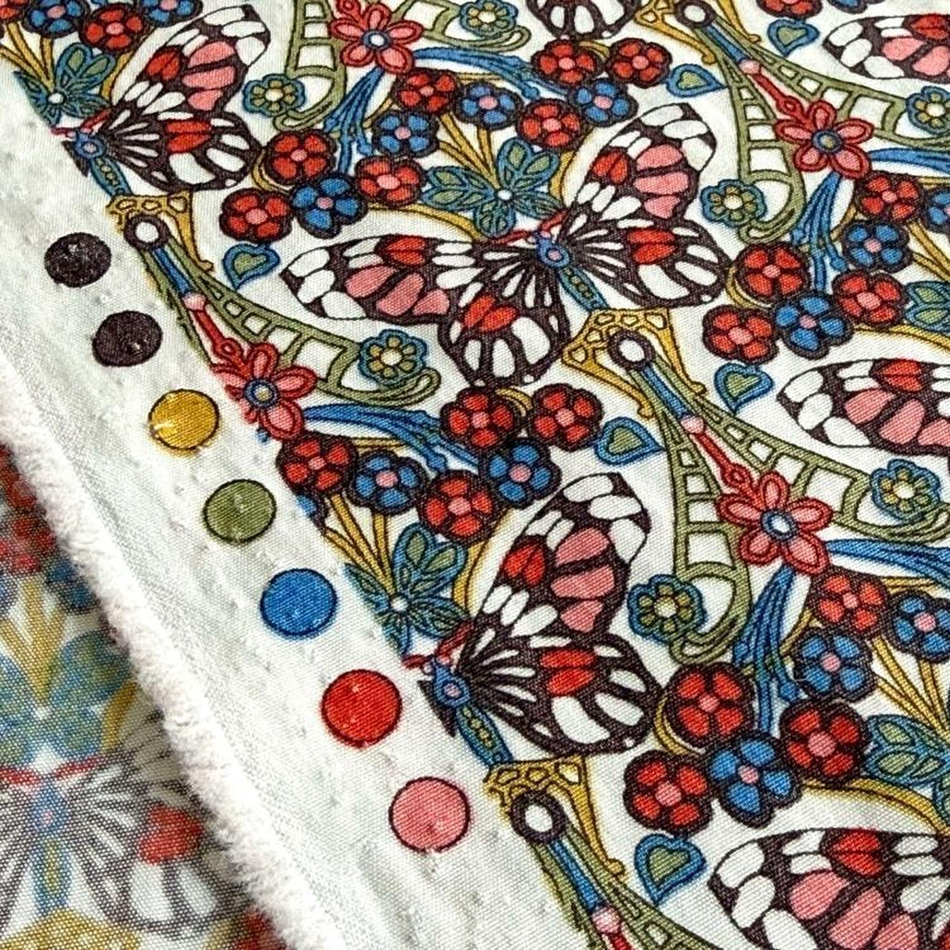 a close-up view of a vibrant, colorful fabric with a repeating pattern of butterflies and flowers. The fabric appears to be a textile, possibly a piece of clothing or a decorative item. The pattern is intricate and detailed, with the butterflies and flowers rendered in a variety of colors, including red, blue, green, and yellow. The fabric is adorned with several small circles, which are likely part of the design or embellishments.
