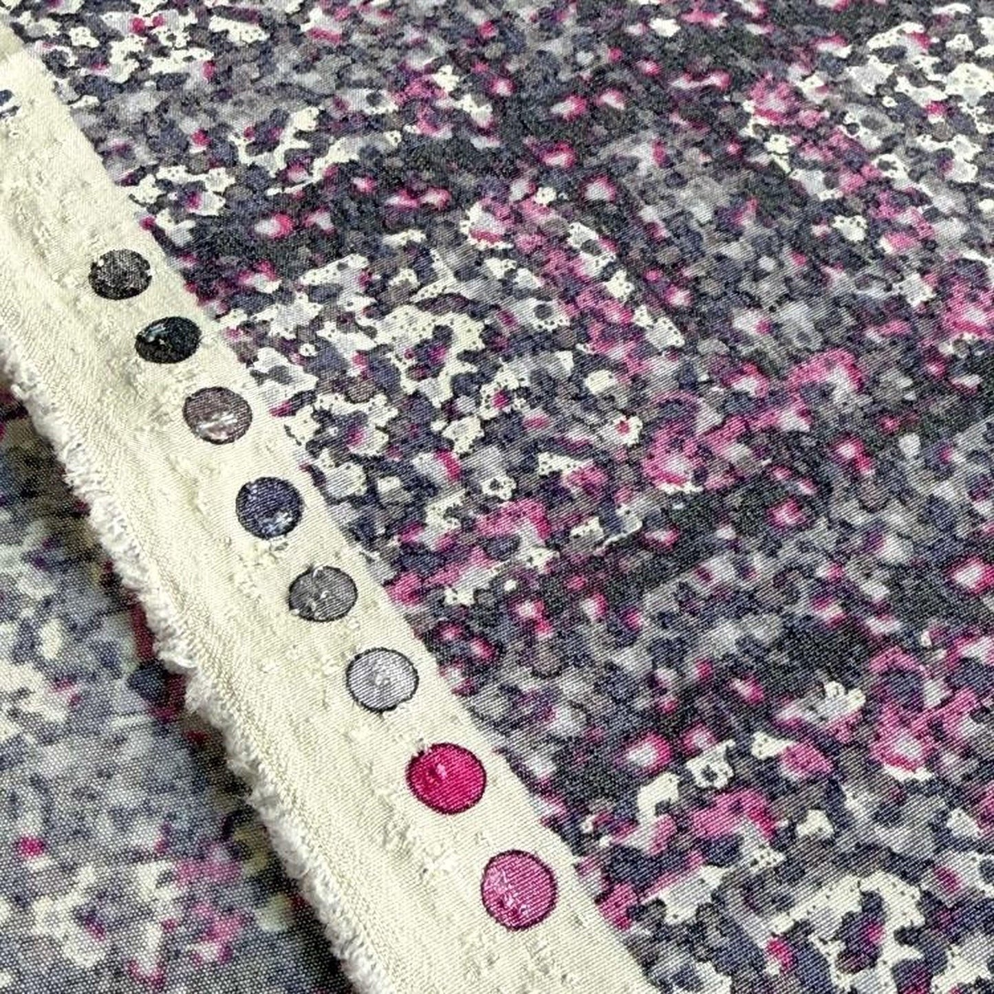 a close-up view of a fabric with a pattern of pink and purple dots, along with a white border.